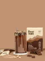 BearWell Whey Chocolate Mousse Sachet Pack next to a glass of chocolate mousse protein smoothie, with the protein powder, empty sachets and blocks of chocolate  surrounding the pack and galss
