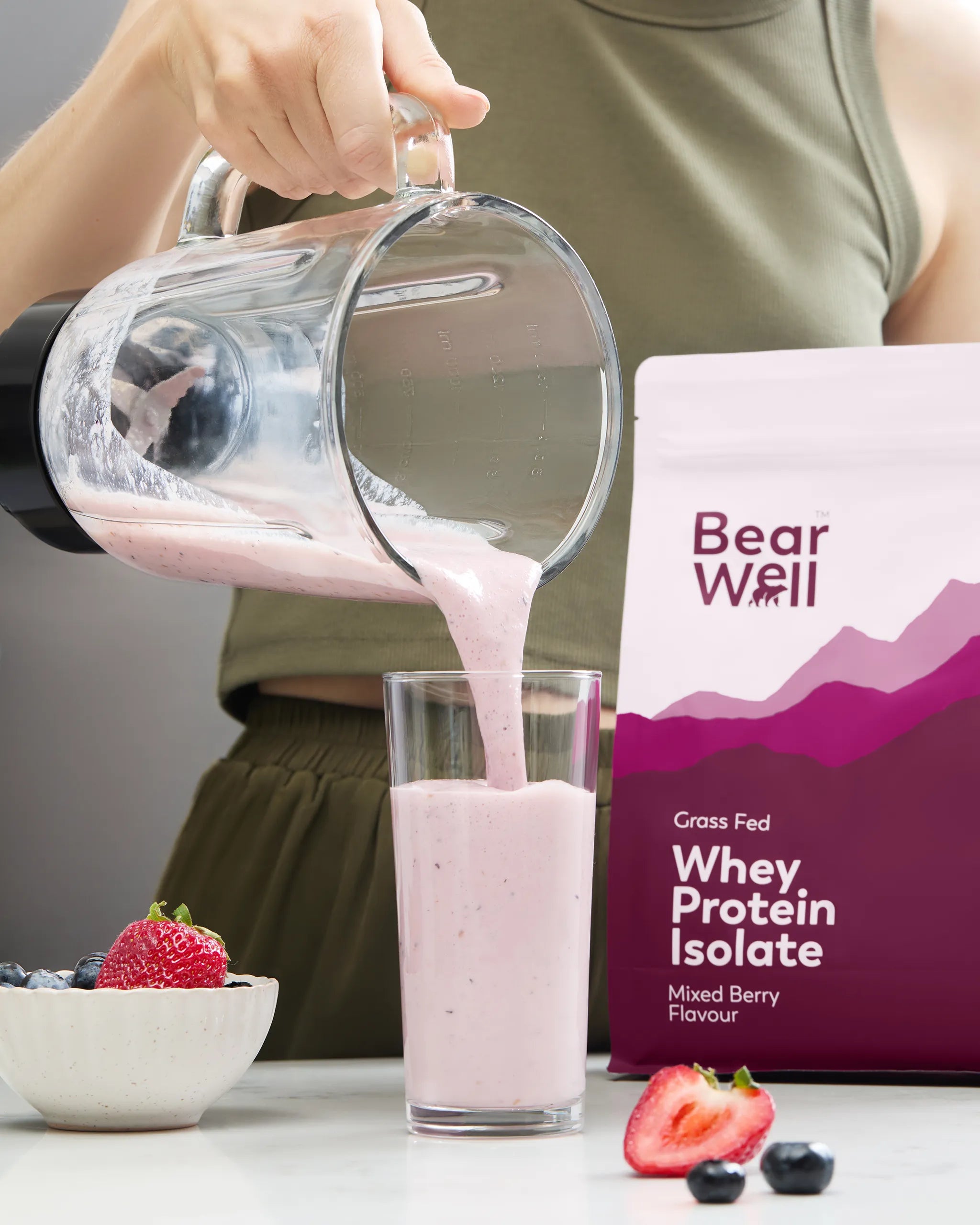 BearWell Whey Protein Isolate, Mixed Berry flavour being poured from a smoothie maker into a glass next to a bowl of fruit