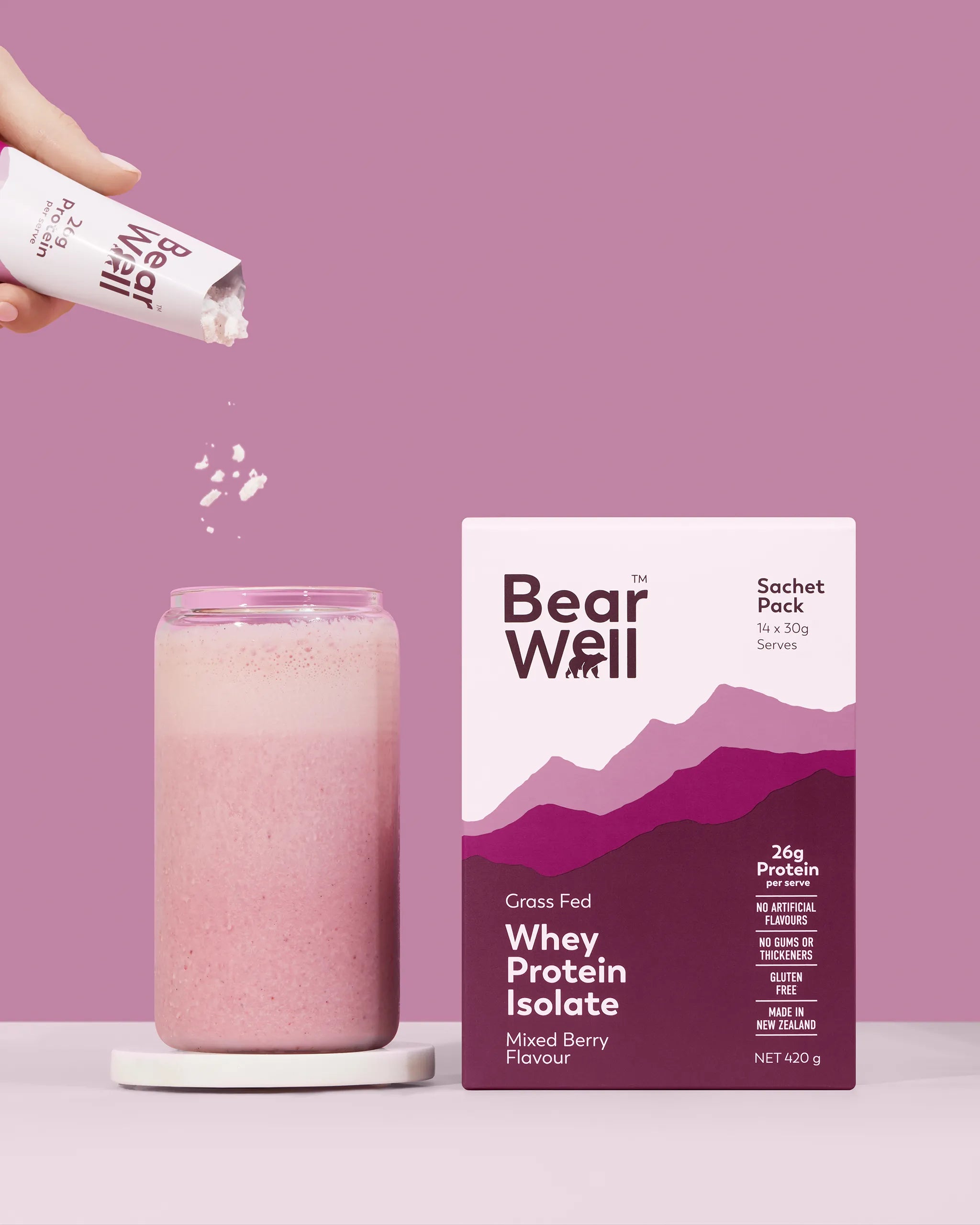 BearWell Whey Protein Isolate Sachet Pack, Mixed Berry flavour with a glass of the protein powder next to it and a customer adding the sachet to the glass with liquid
